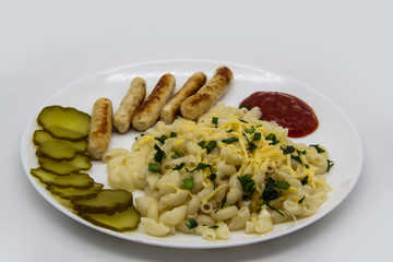 Pasta on a plate with cheese on top and green onions. Delicious pasta made from high quality flour with chicken sausage from grill and sliced cucumber from jar. Horns made of flour cooked with cheese