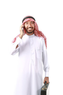 Arab business man wearing keffiyeh, holding a black briefcase and talking on the mobile phone isolated on white background.