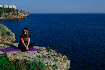 Beautiful young happy girl smiling sitting on rock near sea on a sunny day