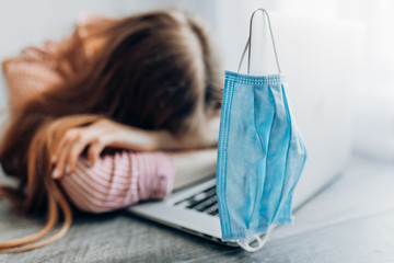 A desperate woman in a protective mask sits at home at a Desk with a computer. The concept of...