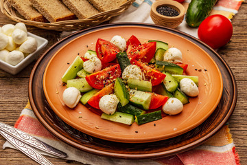 Fresh salad from tomato, cucumber and baby mozzarella. Sunny lunch with crusty bread