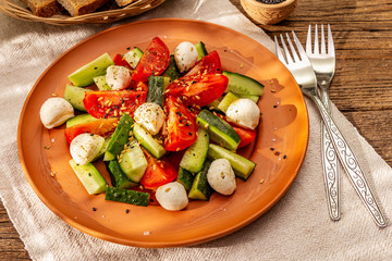 Fresh salad from tomato, cucumber and baby mozzarella. Sunny lunch with crusty bread
