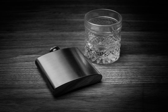 Steel Hip flask resting on table next to glass of whiskey