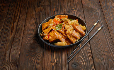 Homemade tofu stir fry with vegetables in hot sweet sauce and pair of chopsticks on dark wooden background and copy space. Asian food concept top view