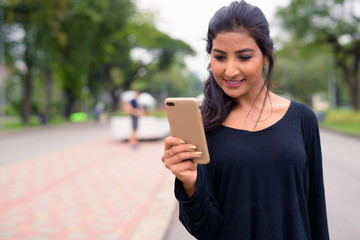 Happy young beautiful Persian woman using phone at the park