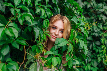 Portrait of a young beautiful woman, hiding in of wild grape leaves.