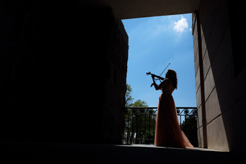 A girl in a long dress plays the violin on the street against a blue sky. Silhouette of a girl....