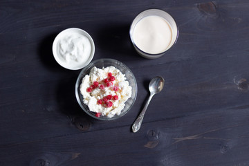 Homemade cottage cheese in bowl with red currant berries, glass of fermented baked milk, sour...