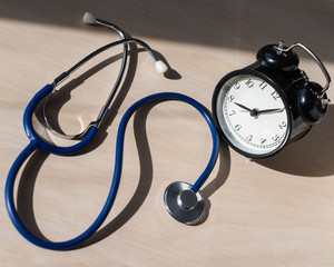 Stethoscope and alarm clock on a wooden table in the sunlight. A tool for measuring blood pressure....
