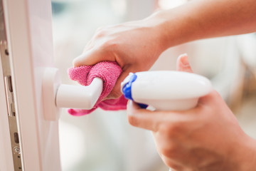 Woman hands cleaning, disinfecting door handle with disinfectant spray and cleaning cloth due to corona virus pandemic. Hygiene concept.