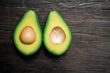 Top view of a ripe avocado halves lying on a wooden background with copy space. One slice with core. Fresh food for a great diet.