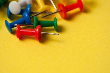 Thumbtacks of different colors on yellow background close-up macro copy space