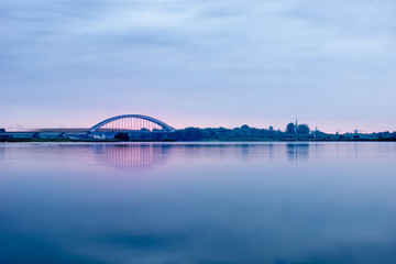 Long exposure of a view on Culemborg The Netherlands over the river Lek with railway bridge and train crossing blue sky and water pink sunrise