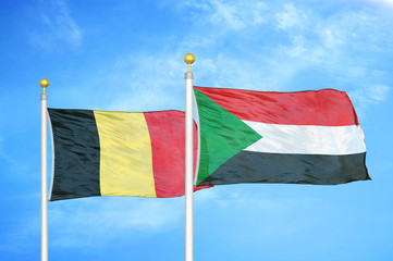 Belgium and Sudan two flags on flagpoles and blue cloudy sky