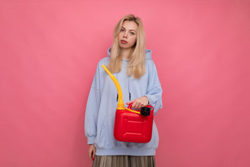 A girl in a hoodie holds a gas canister. The concept of running out of gas on a trip