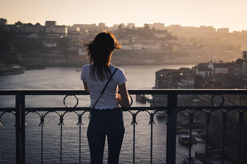 Chica joven de espaldas observando el atardecer desde lo alto del puente Luis I en Oporto