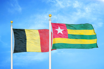 Belgium and Togo two flags on flagpoles and blue cloudy sky