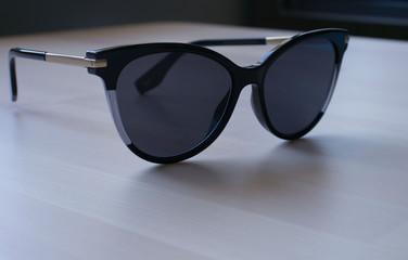 darkened cat-shaped sunglasses lie on the light wooden surface of the table. Elegant, fashionable...