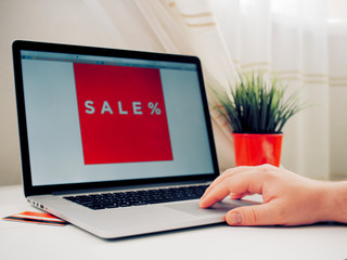 Men's hand at the computer shows a red banner with discounts and sales