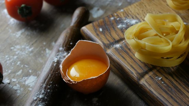 Row of national italian food. Raw flour products close up view. Tagliatelle or fettuccine pastas nests on a wooden kitchen board next to a broken egg yolk in a rustic style