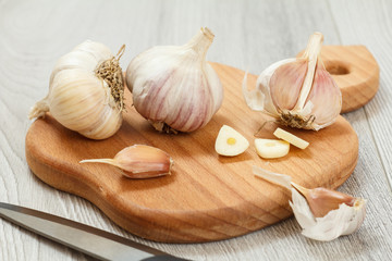 Ripe garlic heads and stainless steel knife on wooden cutting board