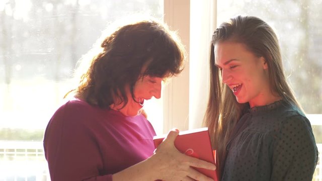 Loving adult daughter presenting spring flowers to happy old mother laughing bonding embracing, young woman congratulating hugging middle aged mom. Mothers day at home