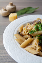 Vegan creamy mushroom garlic pasta with red onions garnished with basil in a white plate with its ingredients in the background, everything on the gray wooden surface