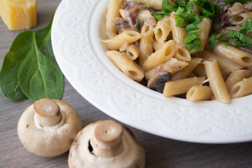 Vegan creamy mushroom garlic pasta with red onions garnished with basil in a white plate with its ingredients in the background, everything on the gray wooden surface
