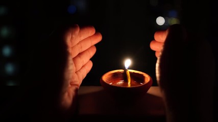 Female hands protecting the flame of diya a small earthenware clay pot lamp with oil and wick from the wind so it keeps burning - Powered by Adobe