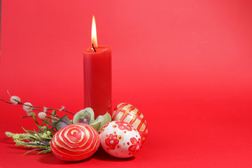 handmade painted Easter eggs with spring branches with buds and a burning candle on a red background