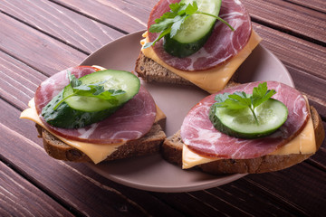 Sandwiches with meat and cheese and green cucumber on a wooden background