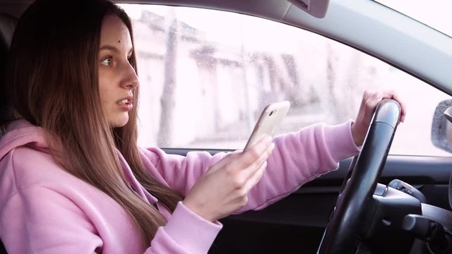Young girl in pink pite speaks on the phone while sitting in a car.