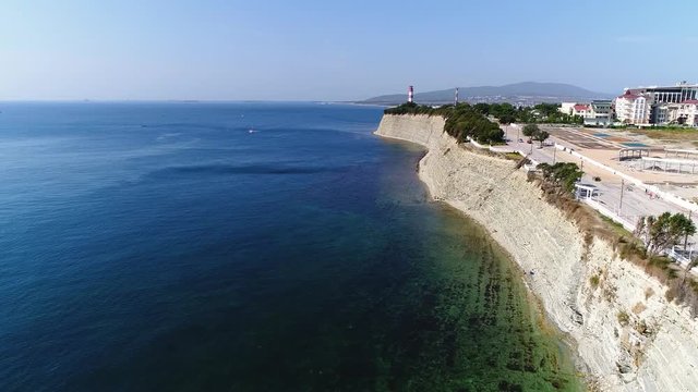 Drone flight along The black sea coastline. High rocky cliff. A strip of shingle beach below. In the distance, the lighthouse of Gelendzhik. 
