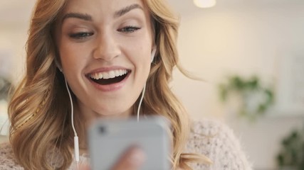 A lovely smiling blonde woman is talking to someone with a video chat while sitting in the white cozy cafe  - Powered by Adobe