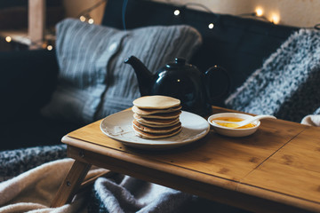 Pancakes with honey on wooden tray in cozy room.