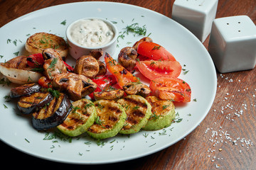 Assorted grilled vegetables - mushrooms, zucchini, peppers, corn in a ceramic plate on a wooden background. Vegetarian warm salad. Healthy food