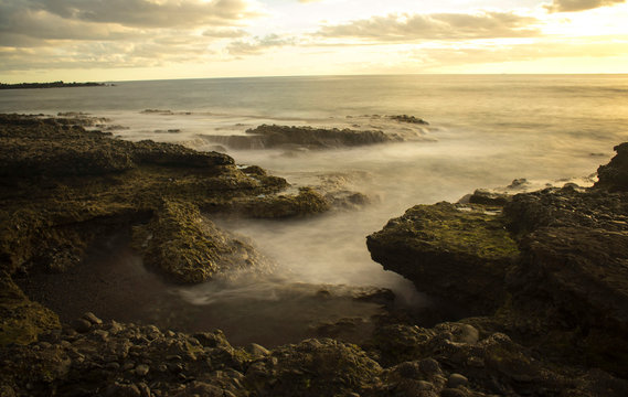 Playa rocosa muestra efecto seda en el mar, durante atardecer.