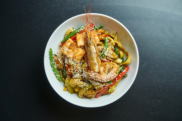Ramen wheat noodles with mussels, shrimps and vegetables fried in a wok in a white bowl on black. Selective focus. Close up. Tasty street food. Seafood