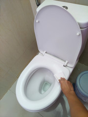 A man's hand uses toilet paper to wipe the toilet lid after the alcohol spray has been disinfected.