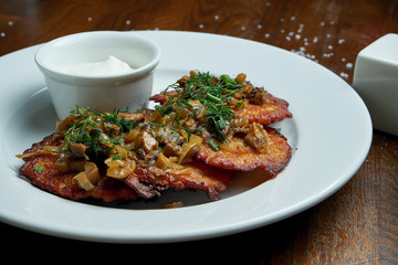 Close up view on Traditional dish of Ukrainian cuisine - potato pancakes with sour cream and mushroom on a white ceramic plate on rustic background