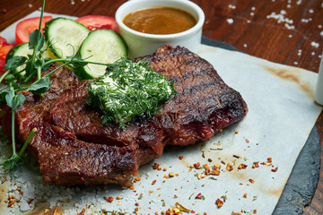 Juicy and mouth-watering grilled ribeye steak with spicy butter on a black tray with a side dish of vegetables. American cuisine.. Close up. Wooden background