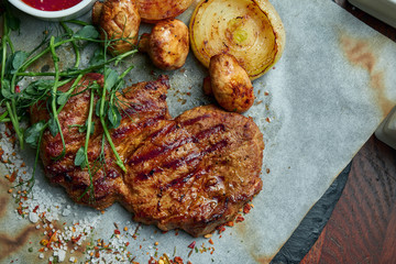 Juicy and mouth-watering grilled ribeye steak with spicy butter on a black tray with a side dish of vegetables. American cuisine.. Close up. Wooden background