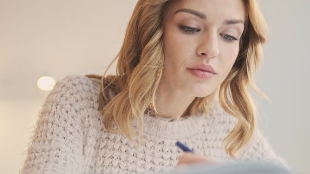 A thinking focused young blonde woman is studying in a cozy place indoors