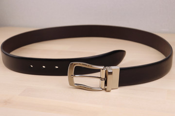 a stylish belt made of smooth black leather and steel fittings lies on a light, wooden background. Expensive gift option for men, women, premium leather, chic performance, handmade, exclusive,