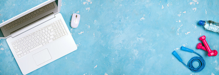 Online fitness workout concept top view. Laptop on the table for stream of sport exercises, dumbbells, jump rope, bottle of water. Copy space