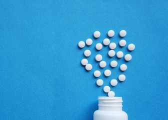 A pile of pills on a blue background. White pills fall out from a white jar on a blue background.