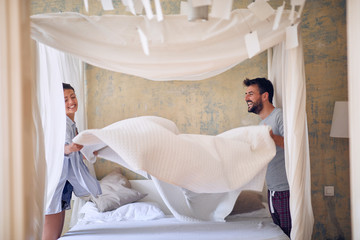 Smiling couple in love making the bed together and having fun. © luckybusiness