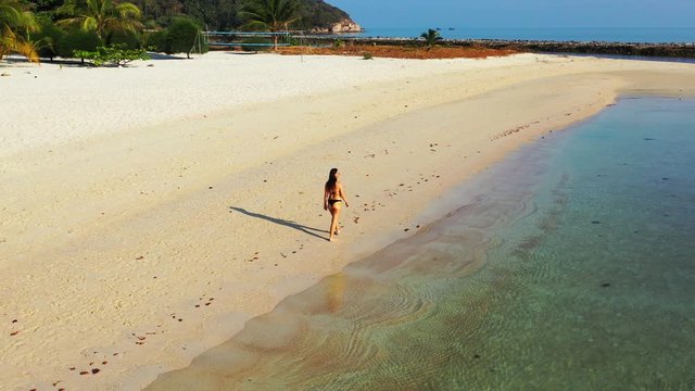 Attractive young woman walking alone on paradise tropical beach with white sand washed by calm turquoise lagoon in Vietnam