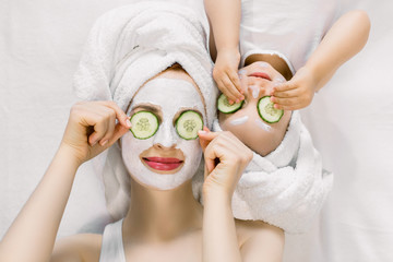 Mom and her 2 years old baby girl having fun together, making clay facial mask and cucumber slices...