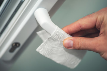 Close-up of man hand over a napkin on a door handle. Bacteria or virus protection concept